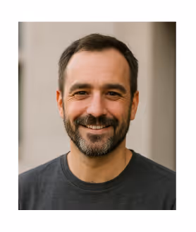 Hombre con barba y cabello corto sonriendo, vestido con camiseta gris oscuro.